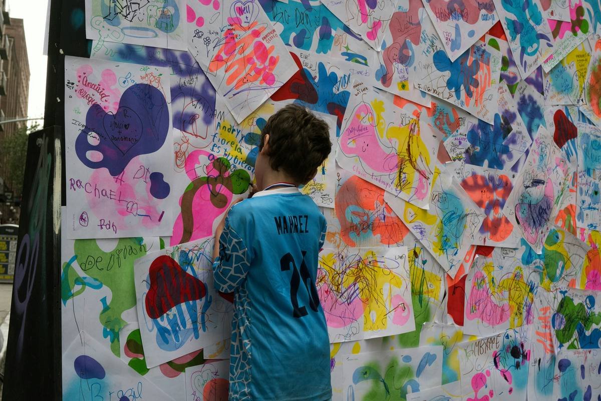 Close-up of child's hand placing a handmade clay dinosaur on an adjustable shelf ledge as part of an art display for kids
